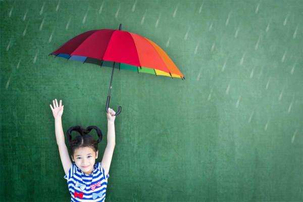 A smiling child with her arms up, holding a colorful umbrella 